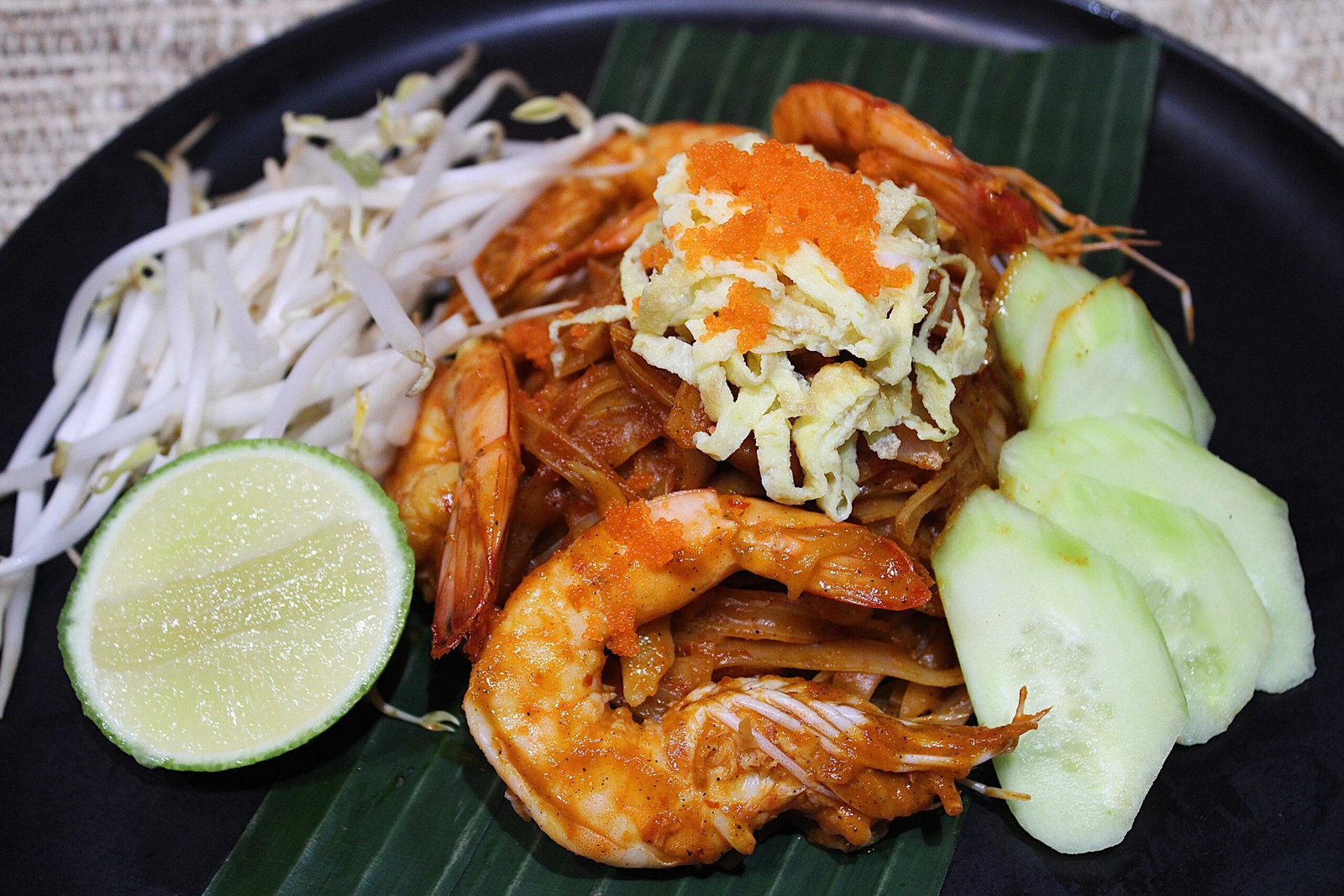 A savory Southern Thai noodle dish, showcasing coconut noodles with succulent shrimp, crisp vegetables and garnished with fresh lime wedges